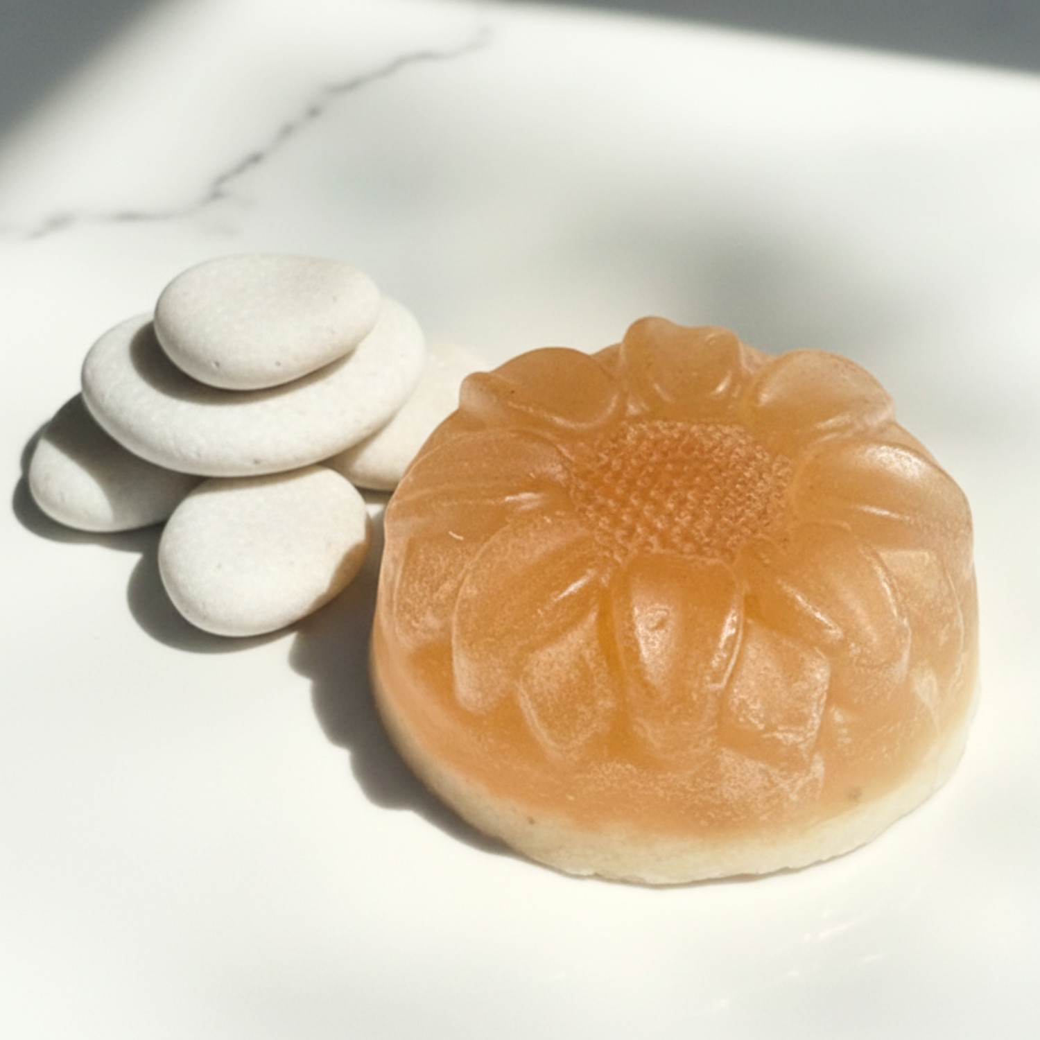 Sunflower-shaped soap on a white marble surface with three small stones.