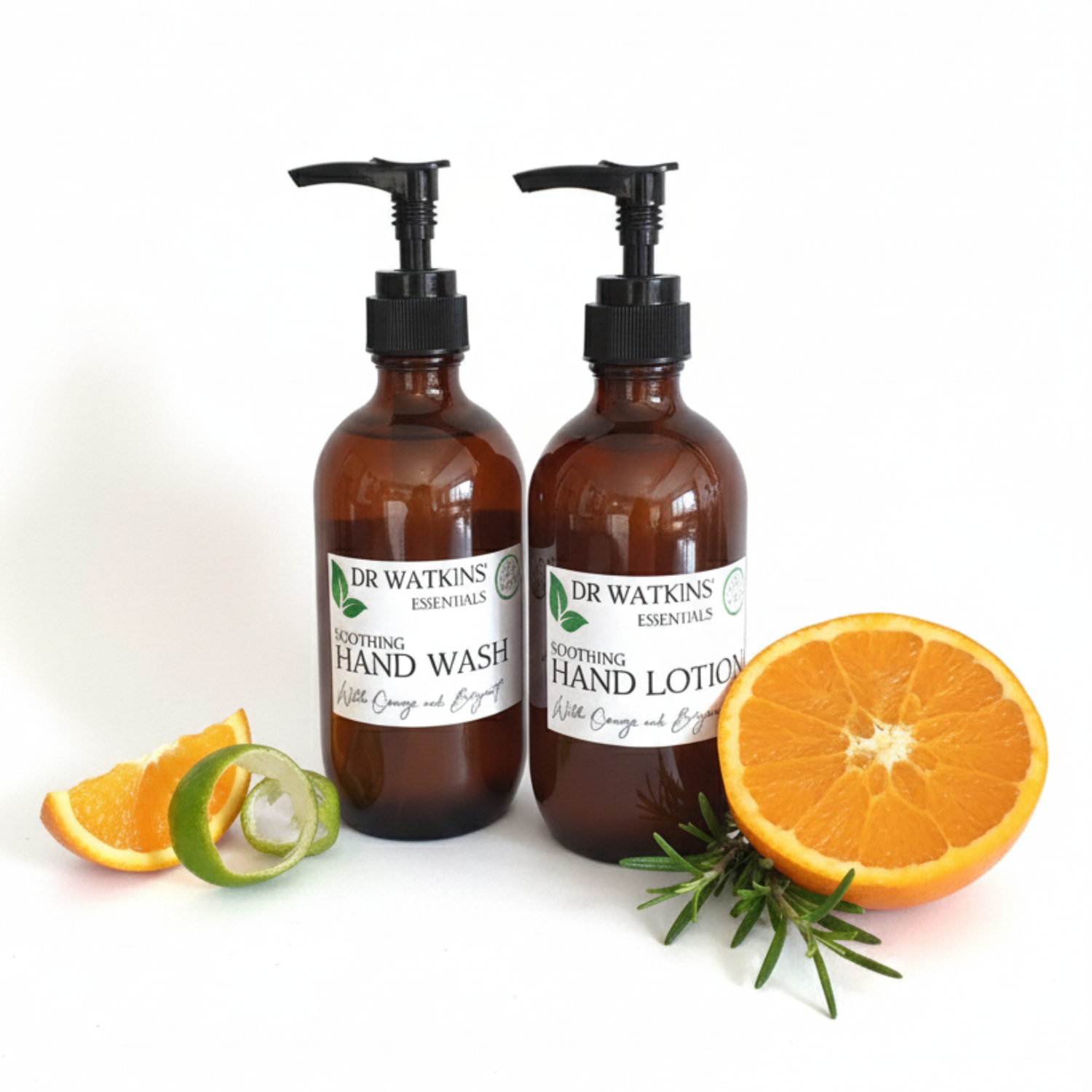 Two brown bottles of Dr. Watkins hand wash and lotion with oranges and rosemary on a white background