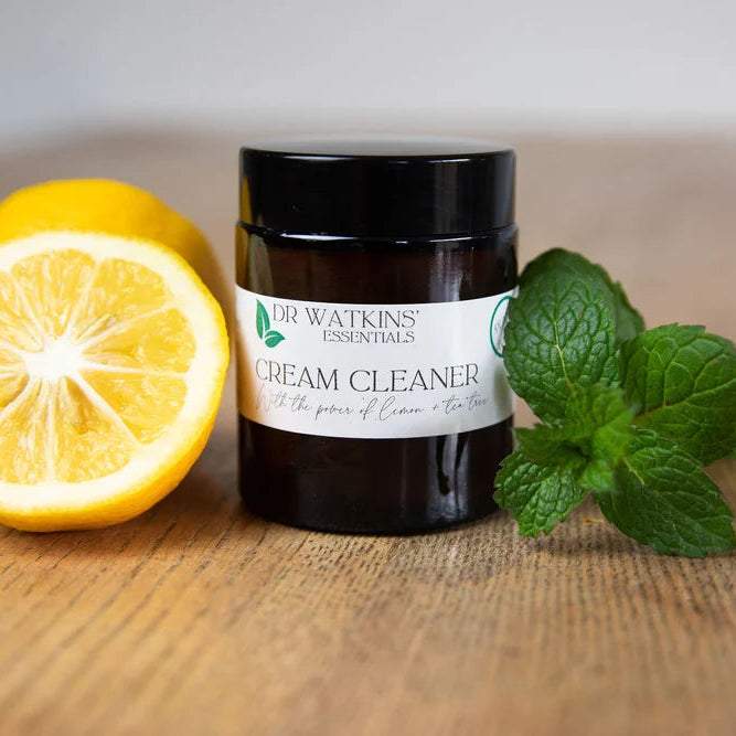 Jar of Dr. Watkins Cream Cleaner with lemons and mint leaves on a wooden surface