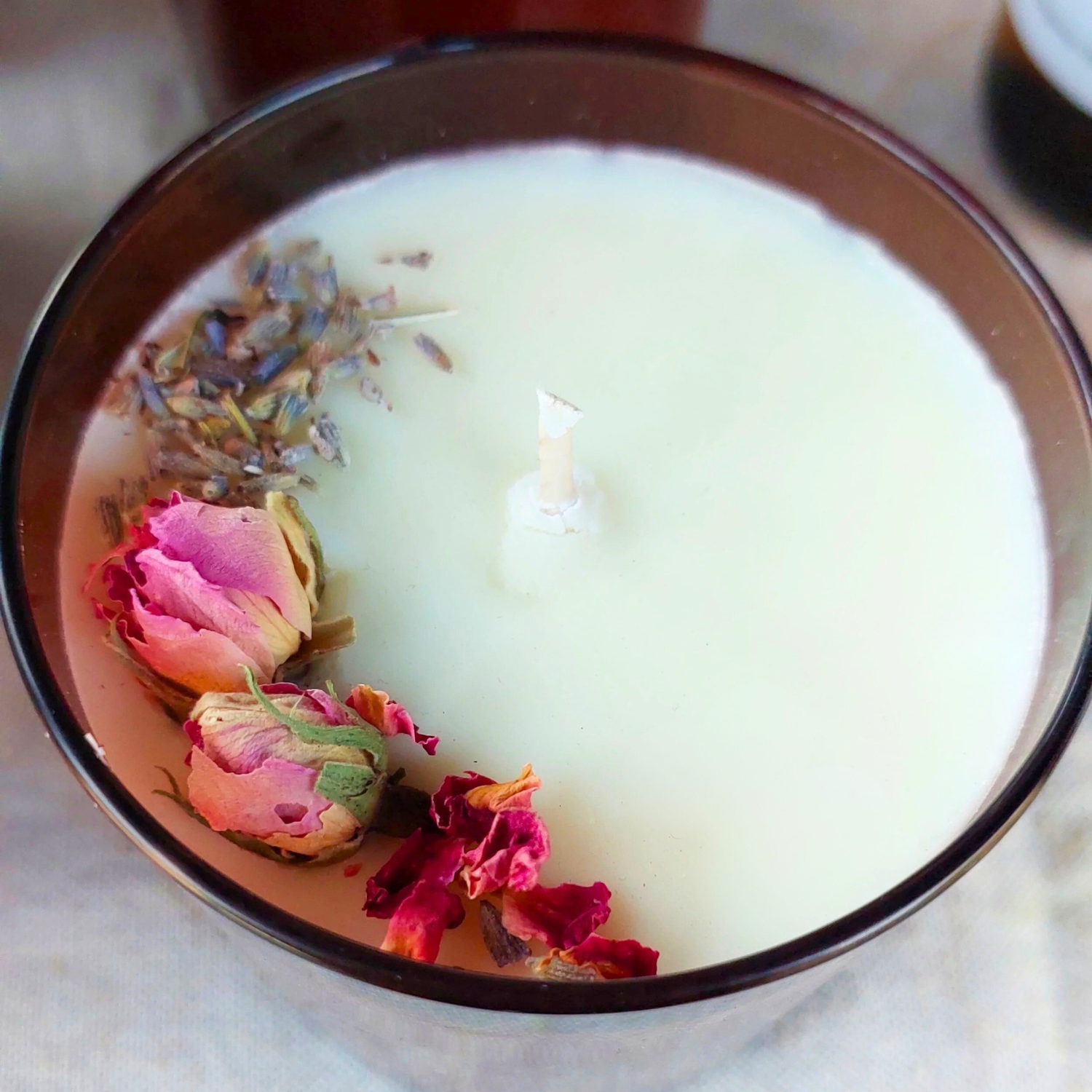 Candle with dried flowers in a glass container on a marble surface